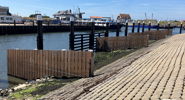 Houten golfbrekers Haven Oudeschild met gebouwen en blauwe lucht