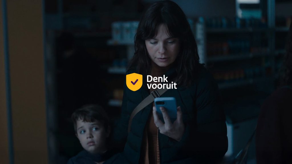 Afbeelding die bij de Denk vooruit-campagne van de overheid hoort (een vrouw staat in het donker met haar zoontje naast zich en kijkt op haar mobiele telefoon)