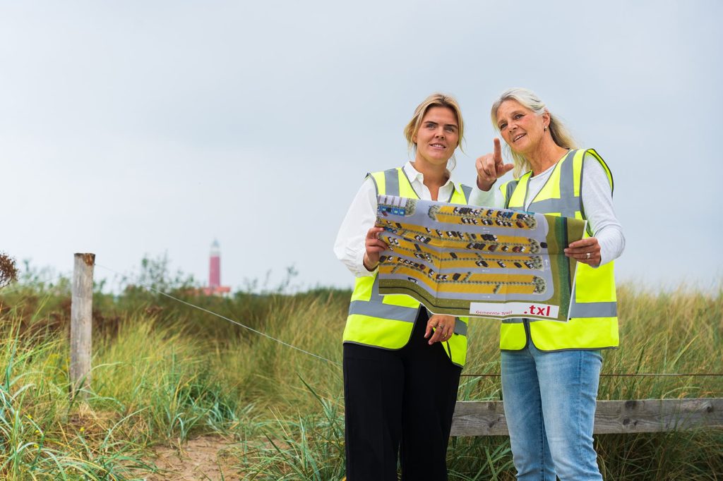 Foto van de campagne over werken op Texel. Twee medewerkers bekijken een overzichtskaart van een parkeerplaats.